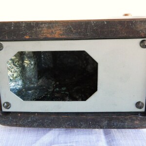 May include: The underside of a wooden box with a white rectangular panel and a cutout in the centre. The panel is held in place with four screws.