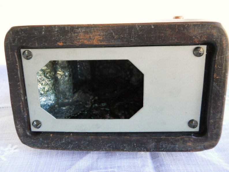 May include: The underside of a wooden box with a white rectangular panel and a cutout in the centre. The panel is held in place with four screws.