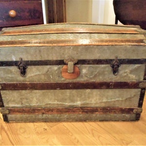 May include: A vintage wooden and metal travel trunk with a distressed finish. The trunk has a hinged lid, metal clasps, and a leather handle.