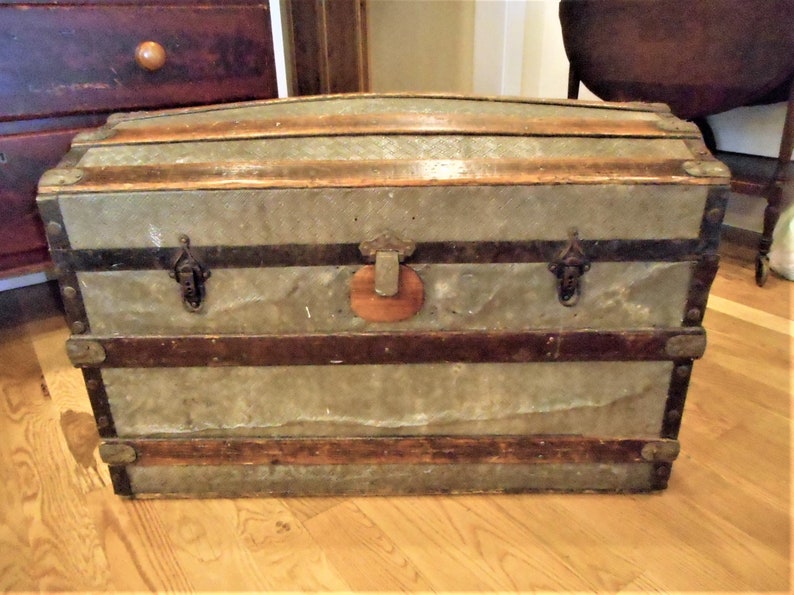 May include: A vintage wooden and metal travel trunk with a distressed finish. The trunk has a hinged lid, metal clasps, and a leather handle.