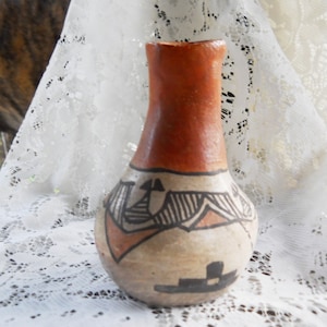 May include: A hand-painted ceramic vase with a brown, black, and white geometric design. The vase has a rounded body and a narrow neck.