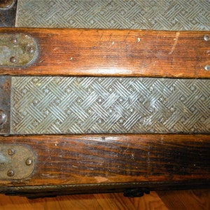 May include: Close-up of a vintage wooden trunk with metal accents. The trunk has a patterned metal surface and is secured with metal clasps.
