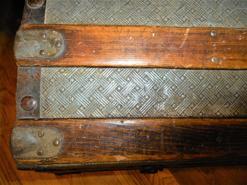 May include: Close-up of a vintage wooden trunk with metal accents. The trunk has a patterned metal surface and is secured with metal clasps.