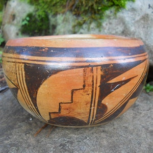 May include: A traditional Native American pottery bowl with a brown and orange geometric design. The bowl is made of clay and has a smooth, polished finish.