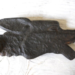 May include: A black cast iron wolf head with a textured surface. The wolf's mouth is open and its teeth are visible. The wolf head is attached to a metal rod.