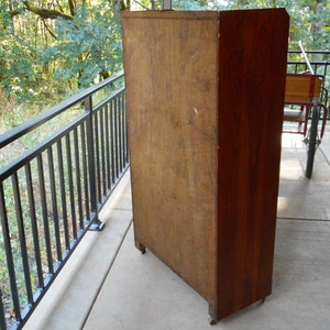 May include: A tall, wooden cabinet with a dark brown finish. The cabinet has a single door and is sitting on a concrete patio.