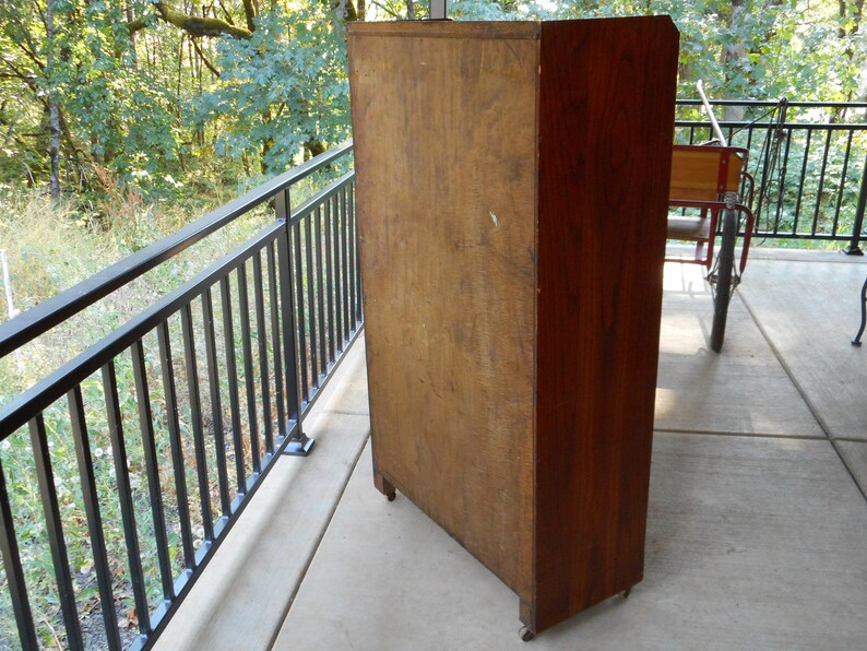 May include: A tall, wooden cabinet with a dark brown finish. The cabinet has a single door and is sitting on a concrete patio.