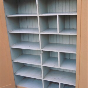 May include: A vintage wooden cabinet with a light brown exterior and a light blue interior. The cabinet has multiple shelves and compartments, perfect for storage.