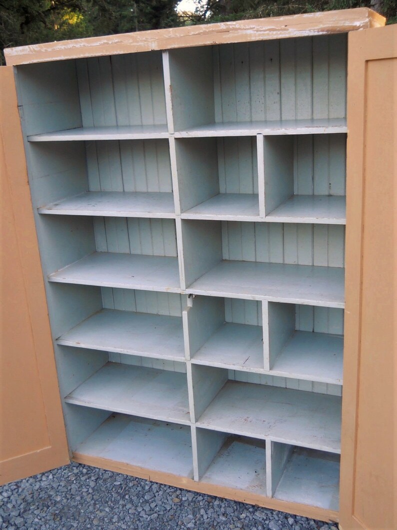 May include: A vintage wooden cabinet with a light brown exterior and a light blue interior. The cabinet has multiple shelves and compartments, perfect for storage.