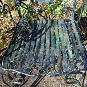 May include: A black metal garden chair with a decorative, ornate design. The chair has a slatted seat and a curved back.