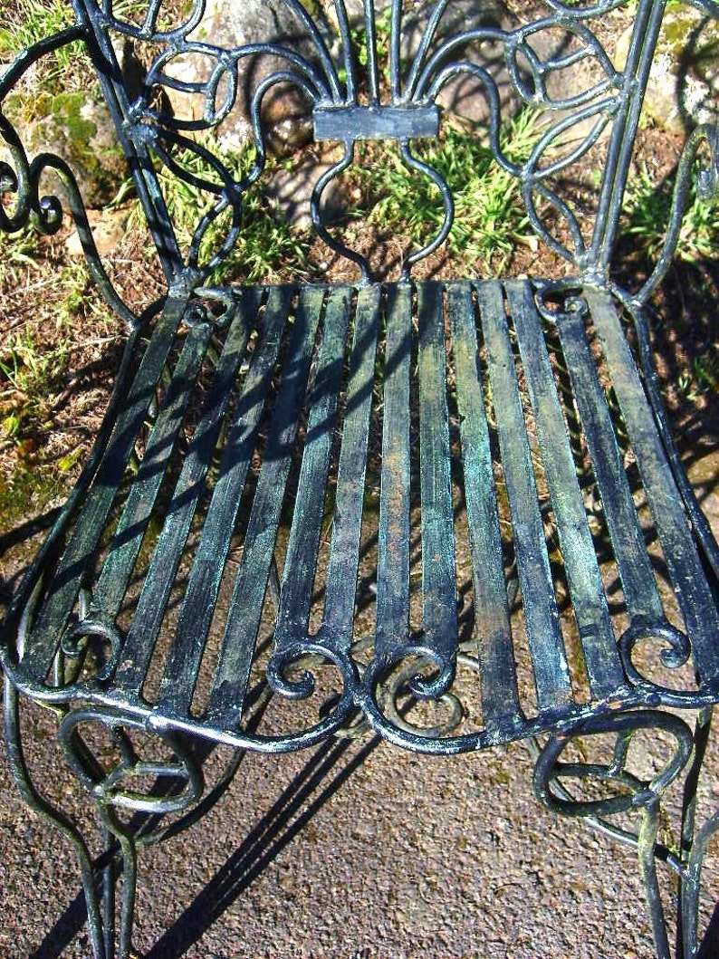 May include: A black metal garden chair with a decorative, ornate design. The chair has a slatted seat and a curved back.