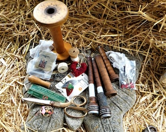 May include: Assortment of vintage wooden bobbins, spools, and a pair of scissors on a stone surface. The bobbins are various shades of brown and have metal accents. The scissors are silver with a wooden handle. There is a small red heart with beads and a piece of white lace in the image.