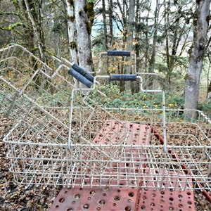 May include: Three white metal wire baskets with black handles. The baskets are stacked on top of each other and are sitting on a red metal surface.