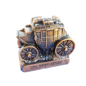 May include: A bronze-coloured metal money box shaped like a stagecoach with wheels. The bank has the text "FIRST FEDERAL SAVINGS 333 HIGH STREET NE SALEM, OREGON" on the base.