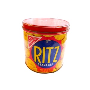 Puede incluir: Una lata roja y amarilla con las palabras "RITZ CRACKERS" y "NET WT. 13 OZ" impresas en ella. La lata está llena de galletas Ritz.