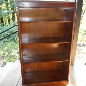 May include: A dark wood bookcase with four shelves and a glass front. The bookcase is on a concrete floor.