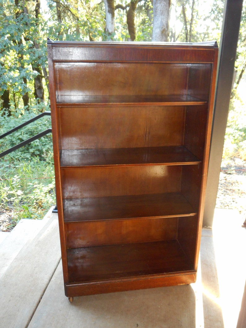May include: A dark wood bookcase with four shelves and a glass front. The bookcase is on a concrete floor.
