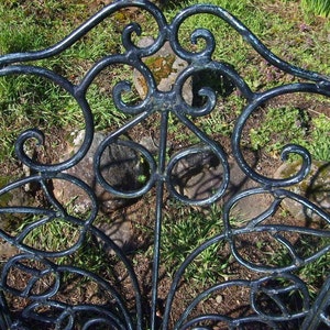 May include: A black metal garden chair with a decorative, intricate design. The chair is made of wrought iron and has a curved back and seat.