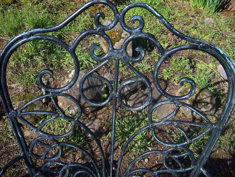 May include: A black metal garden chair with a decorative, intricate design. The chair is made of wrought iron and has a curved back and seat.