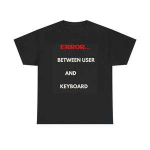 May include: Black t-shirt with the text "ERROR... BETWEEN USER AND KEYBOARD" in a white font, set against a black background. The word "ERROR" is in red, pixelated font.