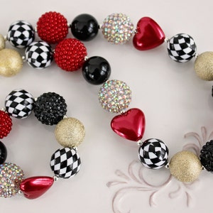 May include: A red, black, white, and gold checkerboard and heart-shaped bead necklace and bracelet set. The necklace and bracelet are made of large, chunky beads.