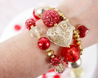 May include: A stack of bracelets with red and gold beads, including a large heart-shaped charm with a gold filigree design.