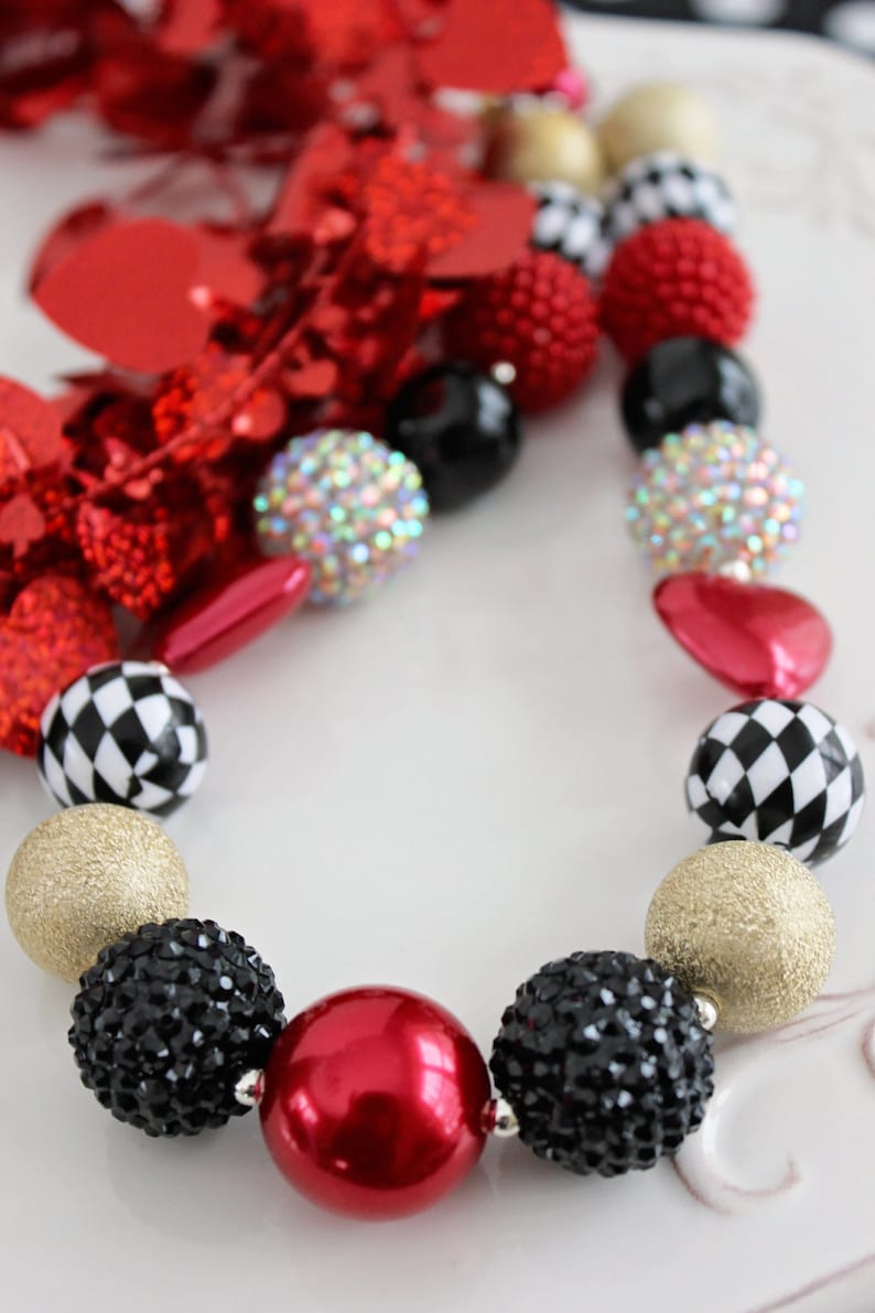 May include: A red, black, gold, and white chunky bead necklace with a checkerboard pattern, rhinestones, and a large red bead.