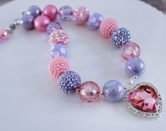 May include: A pink and purple beaded necklace with a large pink rhinestone heart charm. The necklace is made with various sizes and styles of beads, including some with glitter.