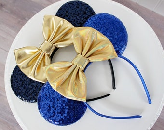 May include: A pair of blue and black sequined mouse ears with gold bows. The headband is blue.