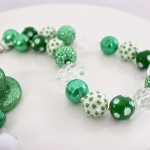 May include: A green and white beaded necklace with shamrock and polka dot patterns. The necklace is made with large, chunky beads and is perfect for a St. Patrick's Day celebration.