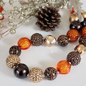 May include: A chunky necklace made of large, colorful beads. The beads are orange, brown, and black with a leopard print pattern. The necklace is perfect for adding a pop of color to any outfit.