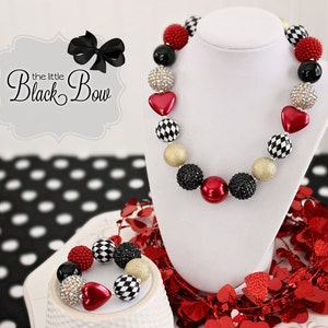 May include: A red, black, and gold checkerboard and heart bead necklace and bracelet set. The necklace and bracelet are made of large, chunky beads.