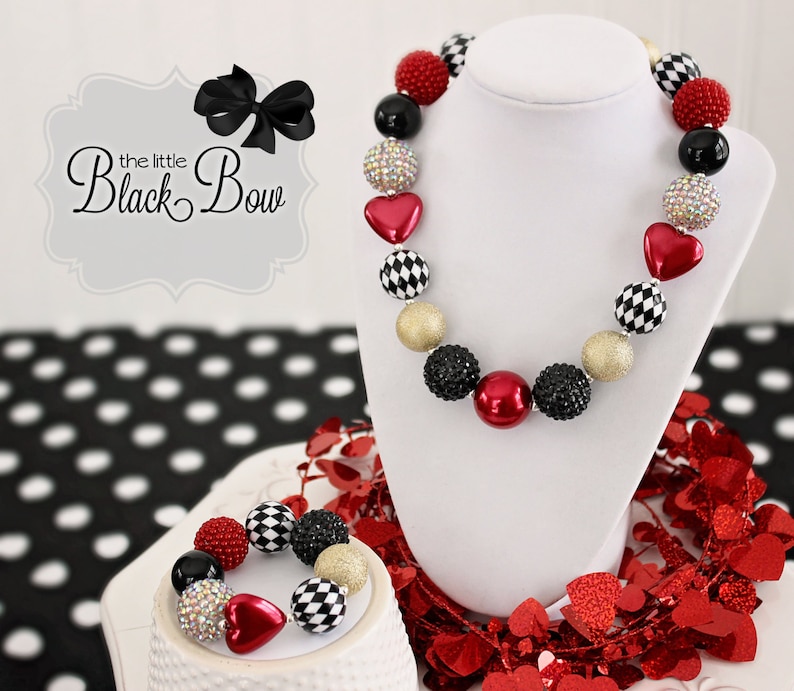 May include: A red, black, and gold checkerboard and heart bead necklace and bracelet set. The necklace and bracelet are made of large, chunky beads.