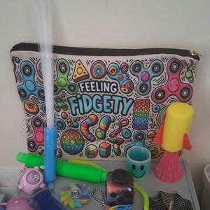 May include: A collection of various colourful fidget toys including a zippered pouch with the text "FEELING FIDGETY" and a pattern of spinners, a fibre optic light wand, a yellow rocket toy, a cube, a blue mesh tube, and several small silicone items.