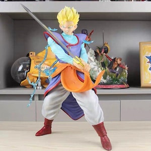 Puede incluir: Una figura de anime coleccionable de un personaje con cabello amarillo puntiagudo, que viste una camisa azul claro de manga larga, una túnica morada con ribete rojo, una faja naranja y pantalones blancos, sosteniendo una espada plateada larga.