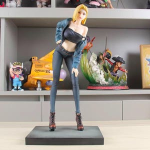 May include: A standing anime-style figurine of a person with short blonde hair, wearing a dark blue denim jacket draped over shoulders, a black ribbed tube top, dark blue skinny jeans, and brown lace-up boots, mounted on a rectangular base.