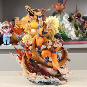 May include: A multi-character Dragon Ball Z action figure set featuring three figures in orange and blue martial arts uniforms, including one with long blonde hair, alongside a large golden dragon, all mounted on a dynamic base with orange energy effects.