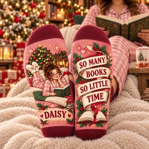May include: A pair of pink and maroon socks featuring a graphic of a person reading a book by a Christmas tree on one side and the text "SO MANY BOOKS SO LITTLE TIME" with a book illustration on the other, personalized with the name "DAISY".