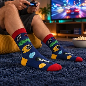 May include: A pair of navy blue crew socks featuring a repeating pattern of colourful icons including green race cars, flaming wheels, blue crystals, and gold coins. The socks have contrasting red cuffs and toe sections, with yellow heel accents.