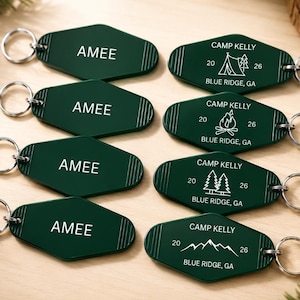 May include: Eight dark green motel-style keychains with silver metal rings. Four keychains feature the name AMEE in white text. The other four feature white graphics of a tent, campfire, pine trees, and mountains with text CAMP KELLY 20 26 BLUE RIDGE, GA.
