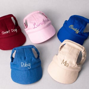 Könnte beinhalten: Fünf Sonnenblenden für Haustiere in Burgunderrot, Hellrosa, Königsblau, Denimblau und Beige. Jede Blende verfügt über einen verstellbaren Riemen und ist mit individuellem Text wie Smart Dog, Luna, Buddy, Ruby und Mia in verschiedenen Farben bestickt.