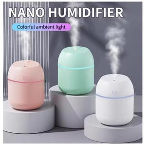 May include: Three portable nano humidifiers in pastel pink, mint green, and white. Each cylindrical device emits a vertical stream of mist and features a thin glowing band. The text NANO HUMIDIFIER and Colorful ambient light appear above.