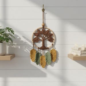 May include: A macrame wall hanging featuring a brown tree of life design centered within a circular wooden hoop. Five crocheted leaf-shaped pendants in shades of mustard yellow and sage green hang from the bottom, accented with small wooden beads.