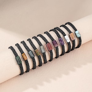May include: A collection of ten adjustable bracelets featuring black braided cord bands. Each bracelet is centered with a single rectangular polished gemstone in various colors, including green, brown, gray, red, purple, white, and blue hues.
