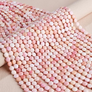 Può includere: Una collezione di piccole perline rotonde e piatte in varie tonalità di rosa, che vanno dal bianco rosato pallido al rosa intenso. Le perline sono disposte in file dense e ordinate, mostrando una superficie liscia e lucida con sottili variazioni di colore.