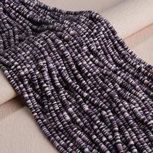 May include: Multiple strands of small, flat, circular beads in shades of deep purple, lavender, and white. The beads are arranged in parallel rows, creating a textured, uniform appearance with a consistent color pattern throughout the collection.