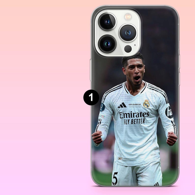 May include: A clear smartphone case featuring a printed graphic of a soccer player wearing a white Real Madrid jersey with the text Emirates Fly Better and the number 5. The case has a cutout for a triple-lens camera system on the back.