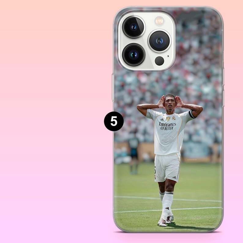 May include: A clear smartphone case featuring a printed image of a soccer player in a white jersey with the text Emirates Fly Better, standing on a green field with hands cupped behind ears. The case has a cutout for a triple-lens camera system.