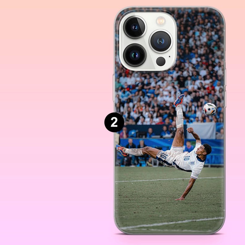 May include: A clear smartphone case featuring a printed graphic of a soccer player in a white uniform performing a bicycle kick on a green field. The player is mid-air with one leg extended upward toward a soccer ball, with a blurred stadium crowd.