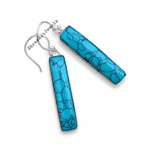 May include: A pair of drop earrings featuring long, rectangular turquoise stones with dark veining set in silver-toned metal frames. The earrings have curved silver ear wires for attachment. The text ShreeArtJewels is visible.